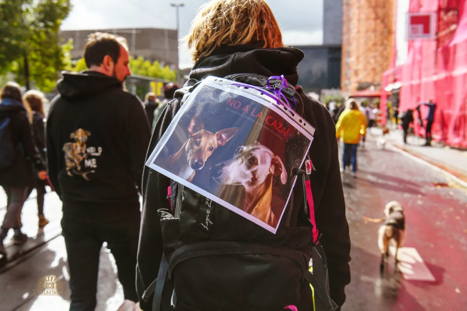 Eine Person von hinten mit einem kleinen Plakat auf dem Rucksack. Auf dem Plakat steht: No a la caza!