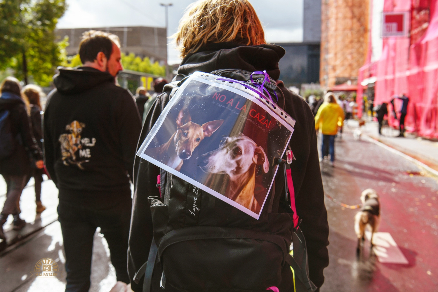 Eine Person von hinten mit einem kleinen Plakat auf dem Rucksack. Auf dem Plakat steht: No a la caza!